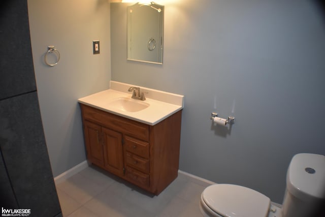 half bath featuring tile patterned floors, vanity, toilet, and baseboards