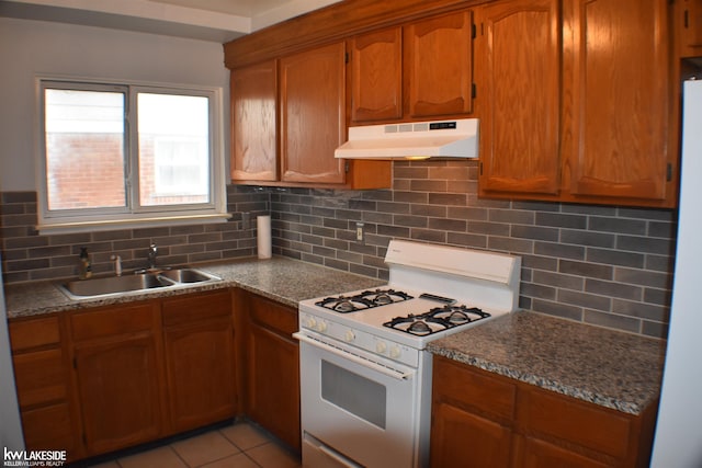 kitchen with light tile patterned floors, fridge, white gas stove, under cabinet range hood, and a sink