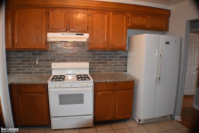 kitchen with under cabinet range hood, stone countertops, white appliances, and brown cabinetry