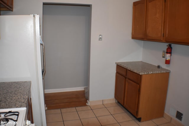 kitchen with light tile patterned floors, visible vents, brown cabinets, and freestanding refrigerator