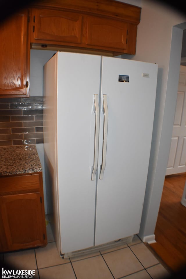 kitchen featuring brown cabinetry, freestanding refrigerator, light tile patterned flooring, and decorative backsplash