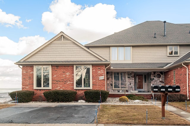 view of front of home featuring stone siding, roof with shingles, a front lawn, and brick siding