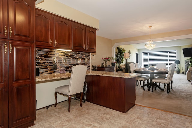 kitchen with a chandelier, light stone countertops, a peninsula, built in study area, and decorative backsplash