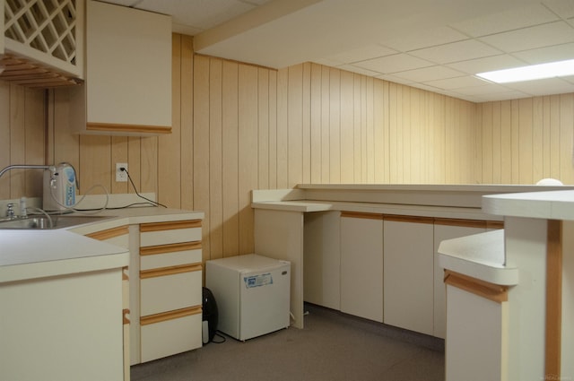 kitchen featuring a drop ceiling, wood walls, a sink, light countertops, and fridge