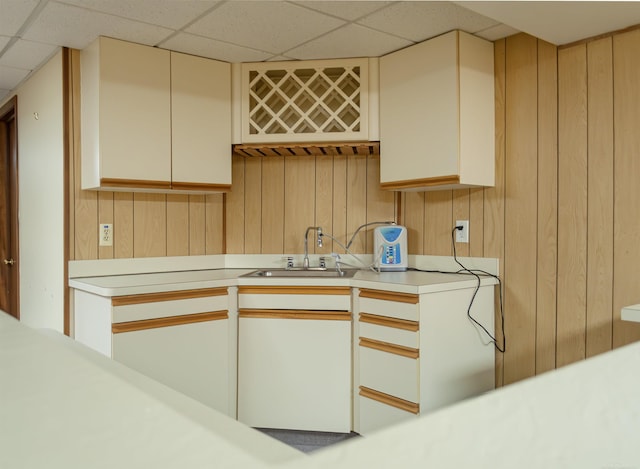 kitchen featuring a drop ceiling, light countertops, cream cabinetry, wood walls, and a sink