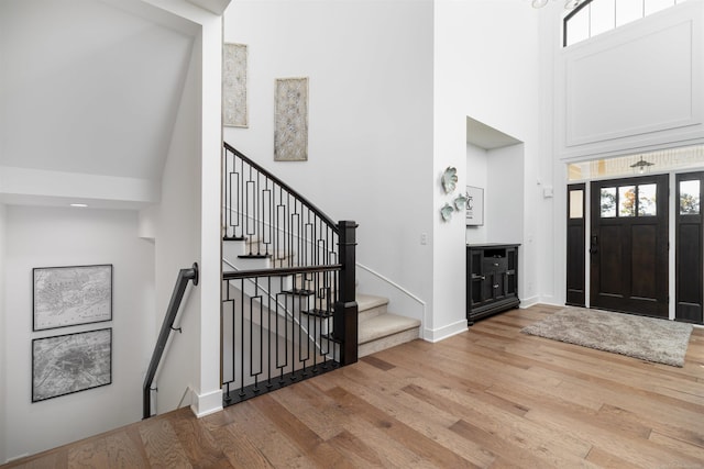 entryway with stairs, wood finished floors, a towering ceiling, and baseboards