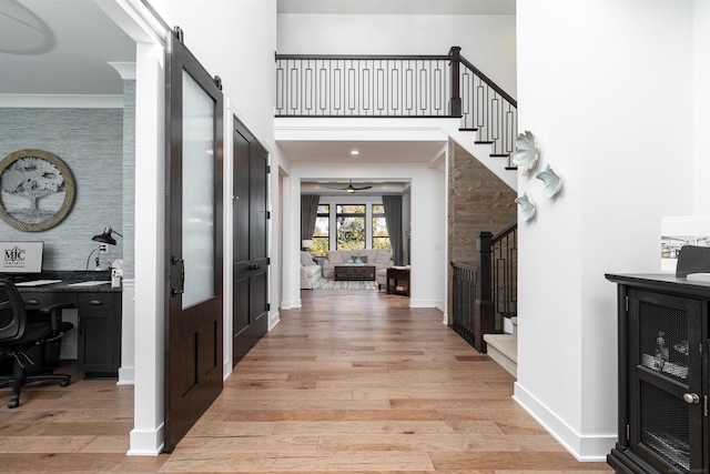 foyer featuring stairway, a high ceiling, a barn door, light wood-style floors, and baseboards