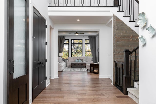 foyer with light wood finished floors, baseboards, a towering ceiling, ceiling fan, and stairs