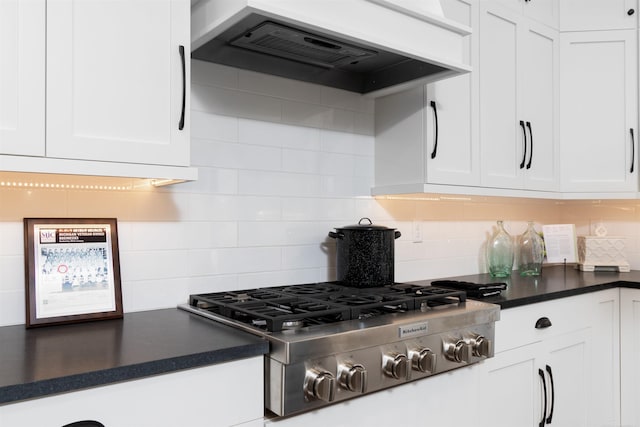 kitchen with dark countertops, custom range hood, stainless steel gas stovetop, backsplash, and white cabinets