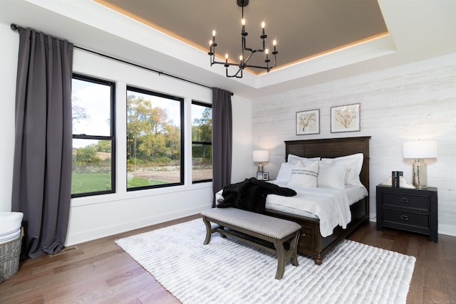 bedroom with a chandelier, wood finished floors, a raised ceiling, and baseboards