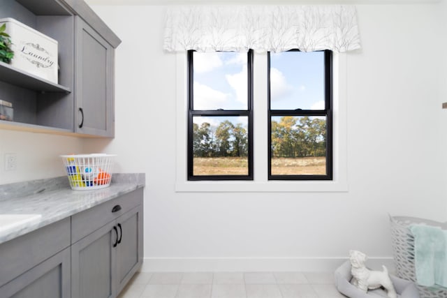 interior space with open shelves, light stone countertops, baseboards, and gray cabinets