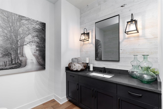 bathroom with wooden walls, wood finished floors, vanity, and baseboards