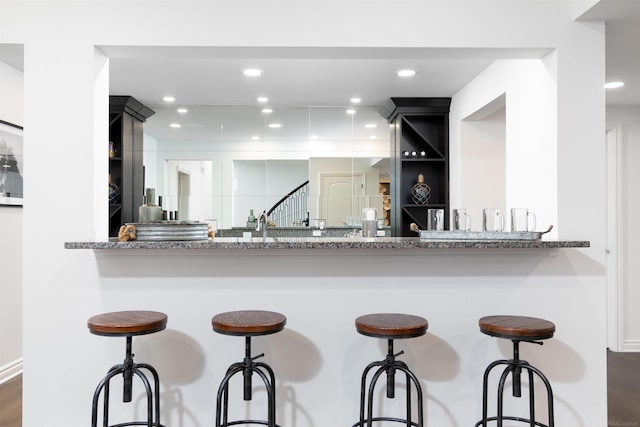 kitchen with dark wood-style flooring, open shelves, recessed lighting, stone countertops, and a kitchen bar