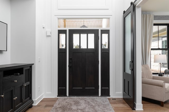 foyer entrance featuring wood finished floors, visible vents, baseboards, and a barn door