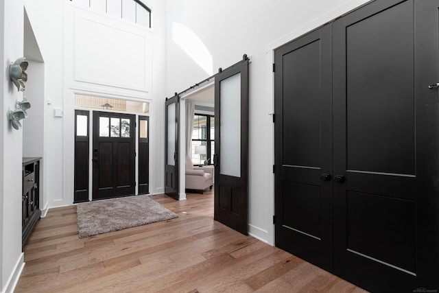 foyer with light wood-style floors, a barn door, a high ceiling, and baseboards