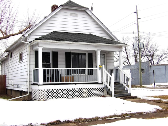 bungalow with a porch, roof with shingles, and a chimney