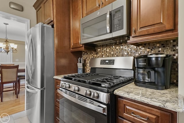 kitchen with light stone counters, brown cabinets, stainless steel appliances, tasteful backsplash, and an inviting chandelier