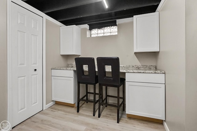 kitchen with light wood finished floors, white cabinetry, light stone counters, and built in study area