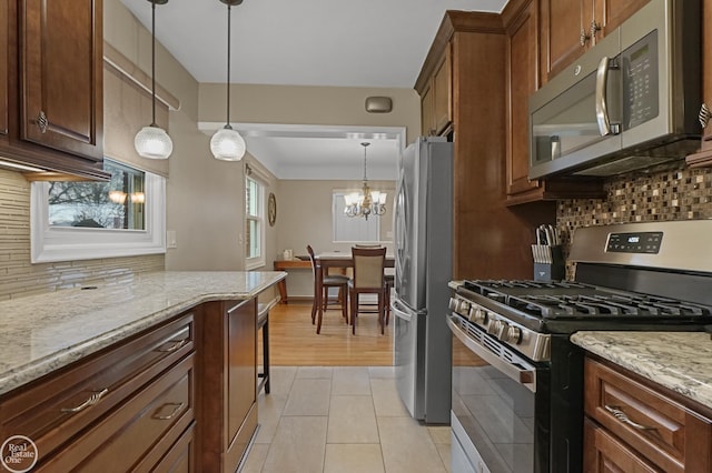 kitchen with stainless steel appliances, pendant lighting, decorative backsplash, and light stone counters