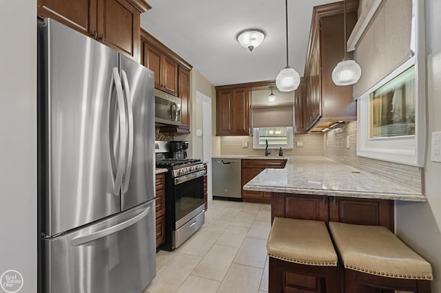 kitchen with a breakfast bar area, light tile patterned flooring, a peninsula, appliances with stainless steel finishes, and tasteful backsplash