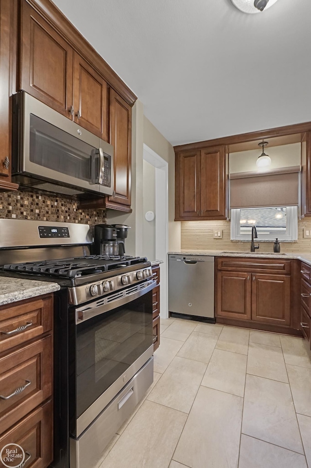 kitchen featuring tasteful backsplash, light stone counters, stainless steel appliances, a sink, and light tile patterned flooring