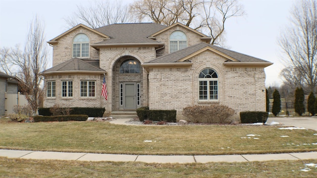 view of front of home featuring a shingled roof, a front lawn, and brick siding