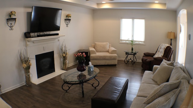 living area featuring a tile fireplace, arched walkways, a tray ceiling, and wood finished floors