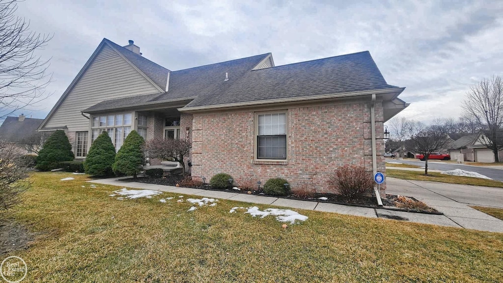 view of front facade with a shingled roof, a chimney, a front lawn, and brick siding