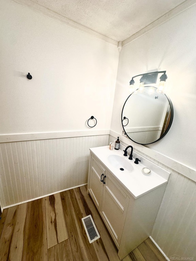 bathroom with a wainscoted wall, visible vents, a textured ceiling, vanity, and wood finished floors