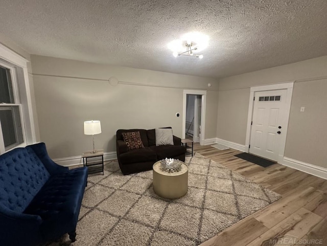 living area with a textured ceiling, wood finished floors, visible vents, and baseboards