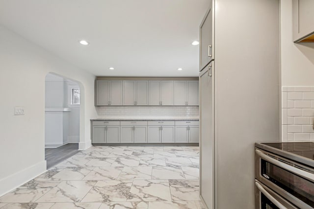 kitchen with arched walkways, marble finish floor, gray cabinets, decorative backsplash, and baseboards