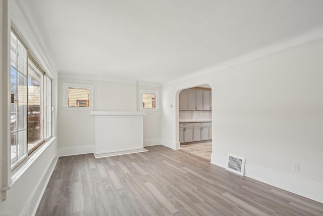 empty room with light wood-style floors, arched walkways, visible vents, and baseboards