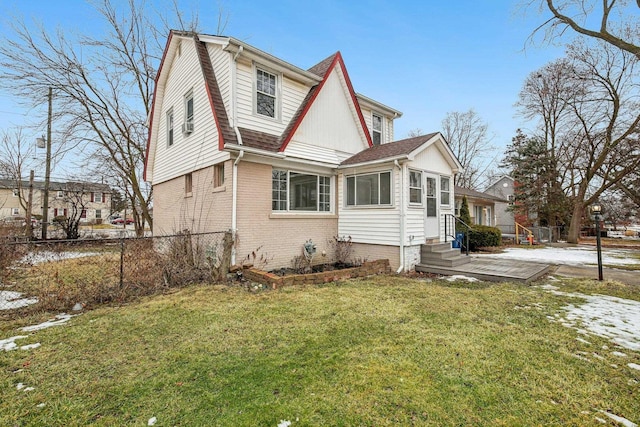 exterior space with entry steps, brick siding, a shingled roof, fence, and a lawn