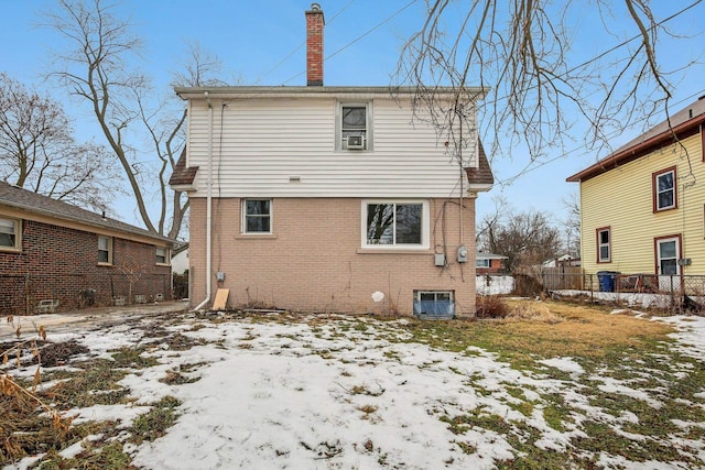 snow covered back of property featuring central AC unit, a chimney, fence, and brick siding