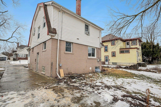 snow covered house featuring brick siding, a chimney, and fence