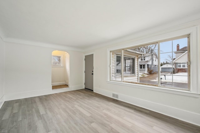 unfurnished room featuring baseboards, visible vents, arched walkways, and wood finished floors