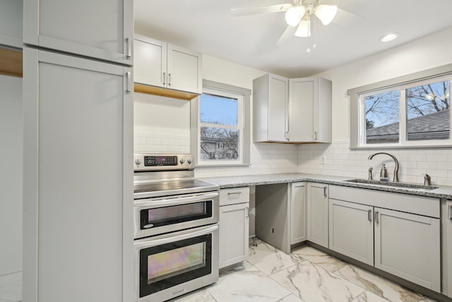 kitchen with marble finish floor, a wealth of natural light, backsplash, a sink, and double oven range