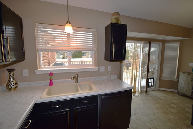 kitchen featuring a sink, light countertops, hanging light fixtures, dishwasher, and stone finish flooring