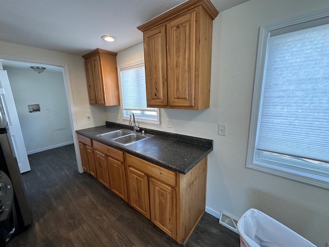 kitchen with dark wood-style floors, brown cabinets, dark countertops, visible vents, and a sink