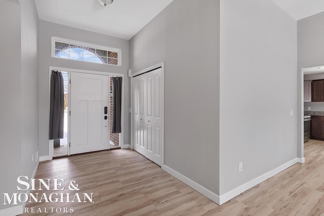 entryway with light wood-style floors, a high ceiling, and baseboards