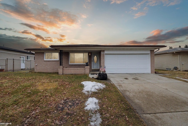 view of front facade with driveway, a lawn, an attached garage, fence, and brick siding