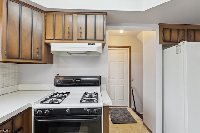 kitchen featuring light countertops, gas stove, freestanding refrigerator, and under cabinet range hood