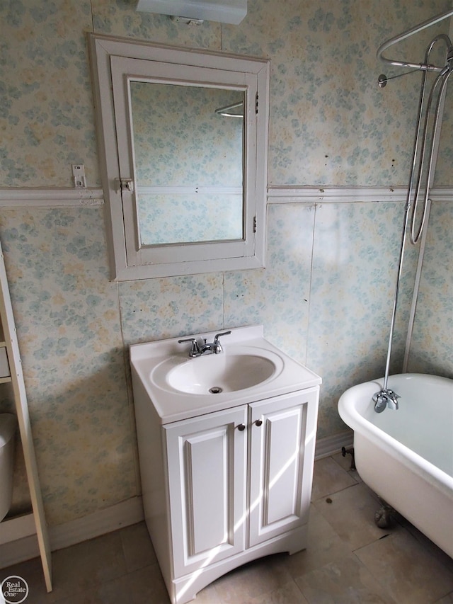 full bath with vanity, baseboards, a freestanding bath, tile patterned floors, and wallpapered walls