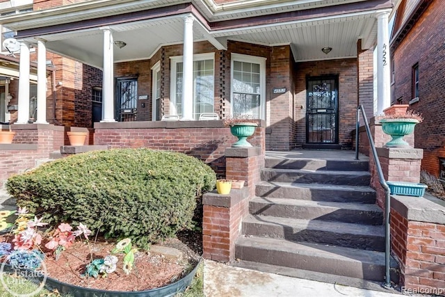 doorway to property with covered porch and brick siding