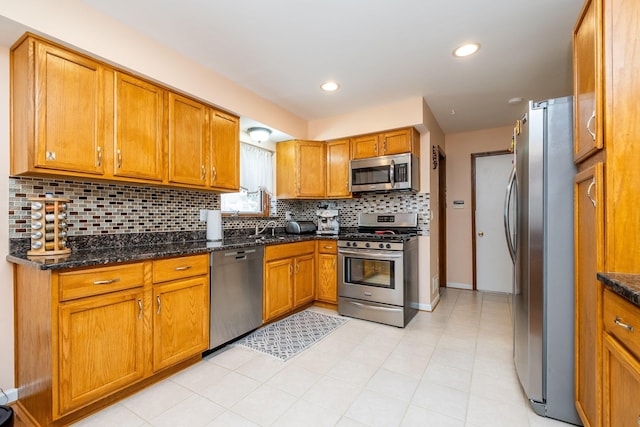 kitchen with tasteful backsplash, appliances with stainless steel finishes, brown cabinetry, and dark stone counters