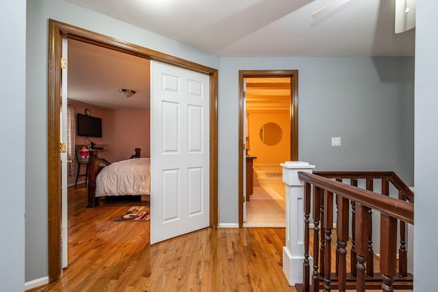 corridor featuring light wood finished floors, baseboards, and an upstairs landing