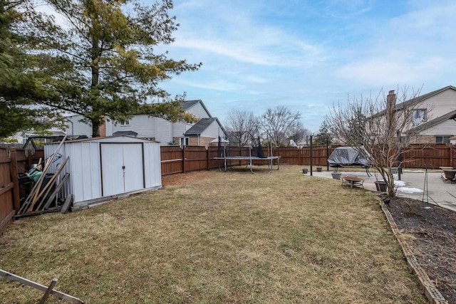 view of yard with a trampoline, an outbuilding, a fenced backyard, and a storage unit