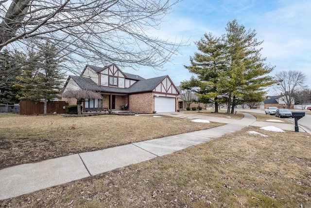 tudor house featuring an attached garage, brick siding, fence, concrete driveway, and a front lawn