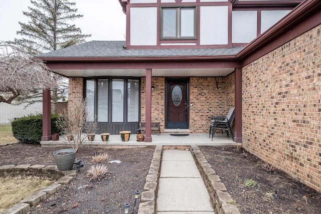 doorway to property featuring brick siding, a porch, and a shingled roof