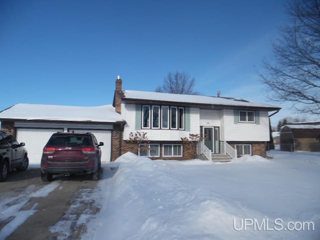 raised ranch featuring entry steps, brick siding, a chimney, and an attached garage